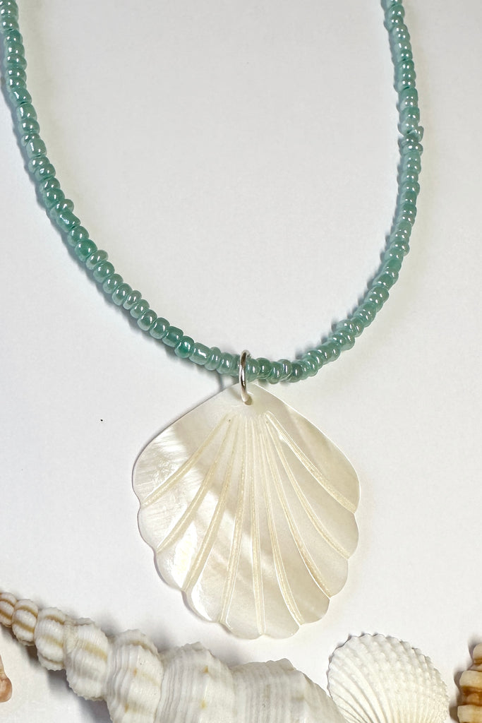 this scallop shape hand carved from Mother of Pearl shell all carry the distinctive marks of the artist who created them, no two shells are ever alike,  strung on pearlescent pale blue glass beads.