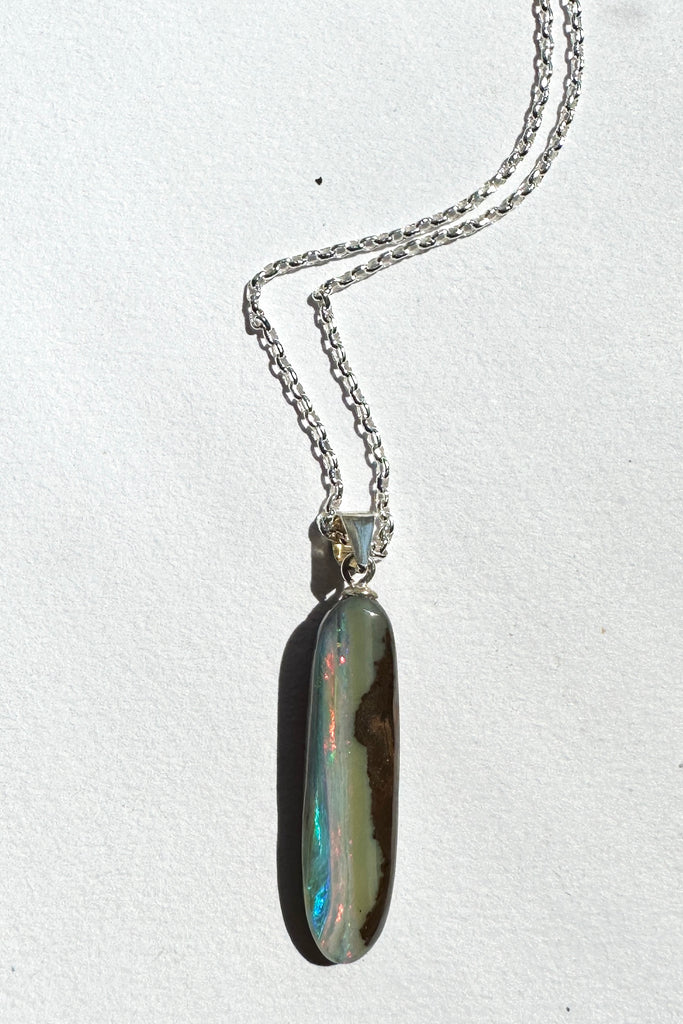 This intriguing opal pendant has been cut leaving the boulder rock on one side, on the other is a river of bright pink and some blue running from top to bottom. The back and front have been polished to a good shine. Opal is 3.5cm long.
