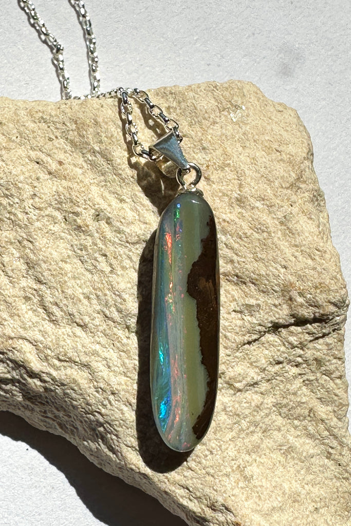 This intriguing opal pendant has been cut leaving the boulder rock on one side, on the other is a river of bright pink and some blue running from top to bottom. The back and front have been polished to a good shine. Opal is 3.5cm long.