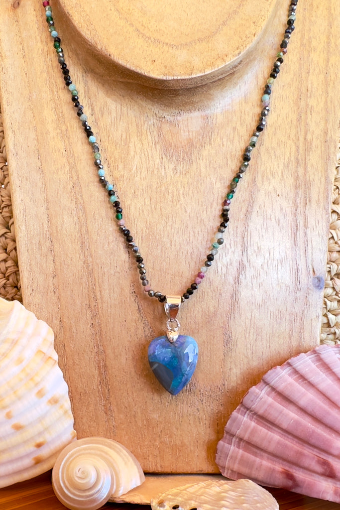 An Australian solid boulder opal pendant in a heart shape, a stunning and rather mystical piece with bright green rivers and blue pools against an almost black ground. Detail that reveals bright flashes of blue green and dark blue. 