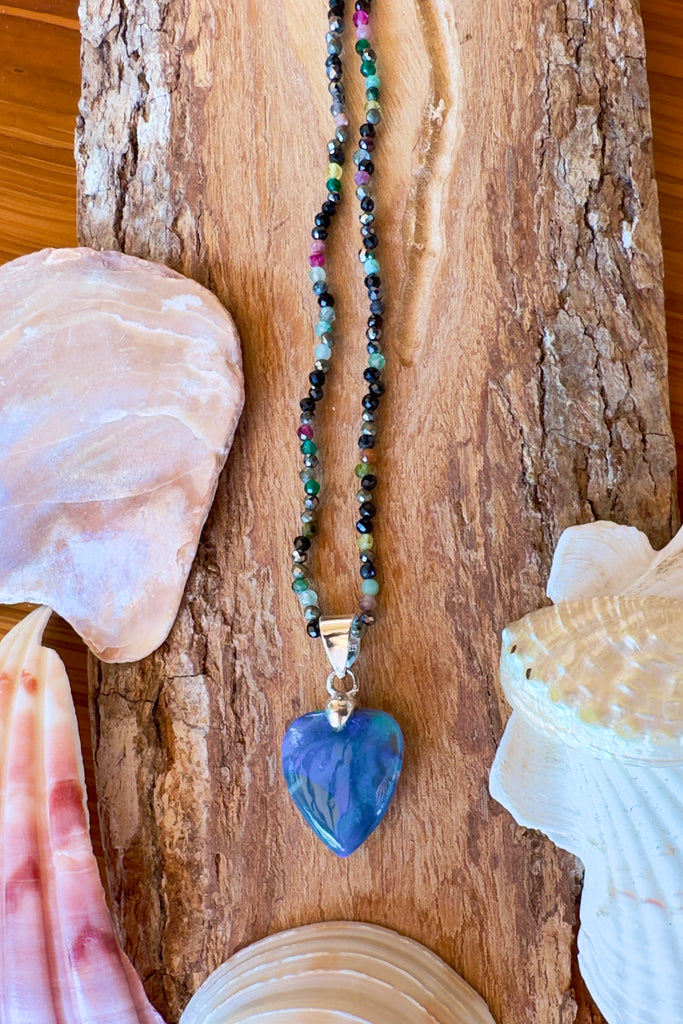 An Australian solid boulder opal pendant in a heart shape, a stunning and rather mystical piece with bright green rivers and blue pools against an almost black ground. Detail that reveals bright flashes of blue green and dark blue. 