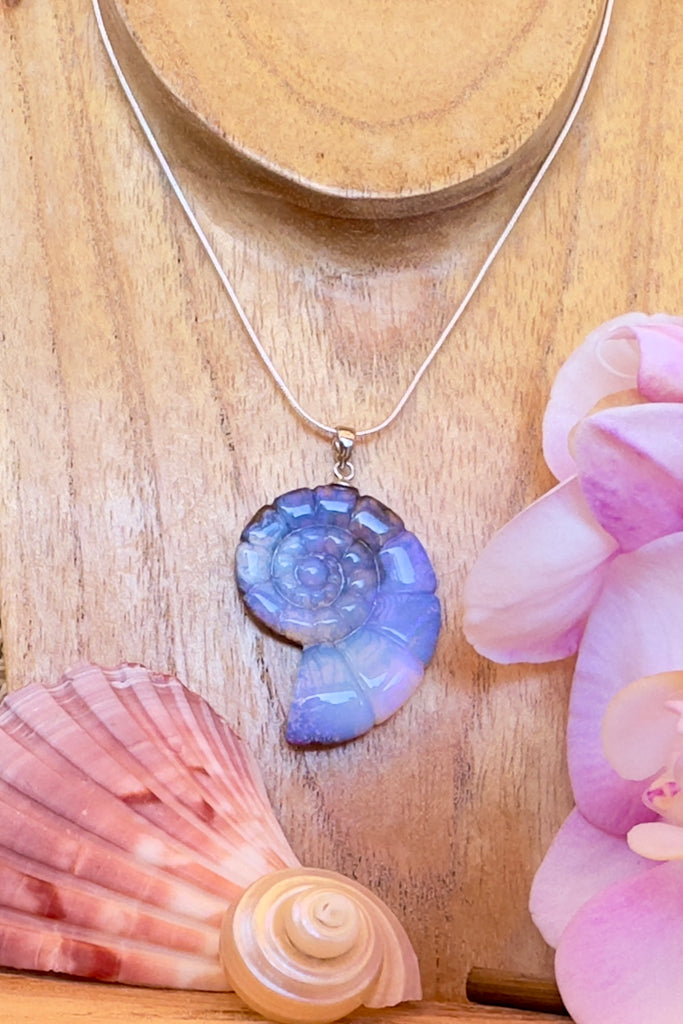 An Australian solid boulder opal pendant in the shape of a Nautilus sea shell, it has deep crystalline detail in mauve, purple and blue with slight flashes of pink. The back of the heart is polished boulder stone.