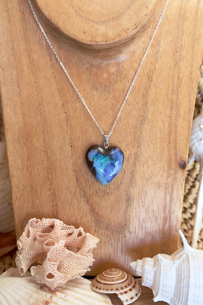 From our range of Australian opal pendants, an Australian solid boulder opal pendant in a heart shape, with crystalline detail that reveals bright flashes of blue green, dark blue and misty mauve. This piece has been cut into a soft heart shape