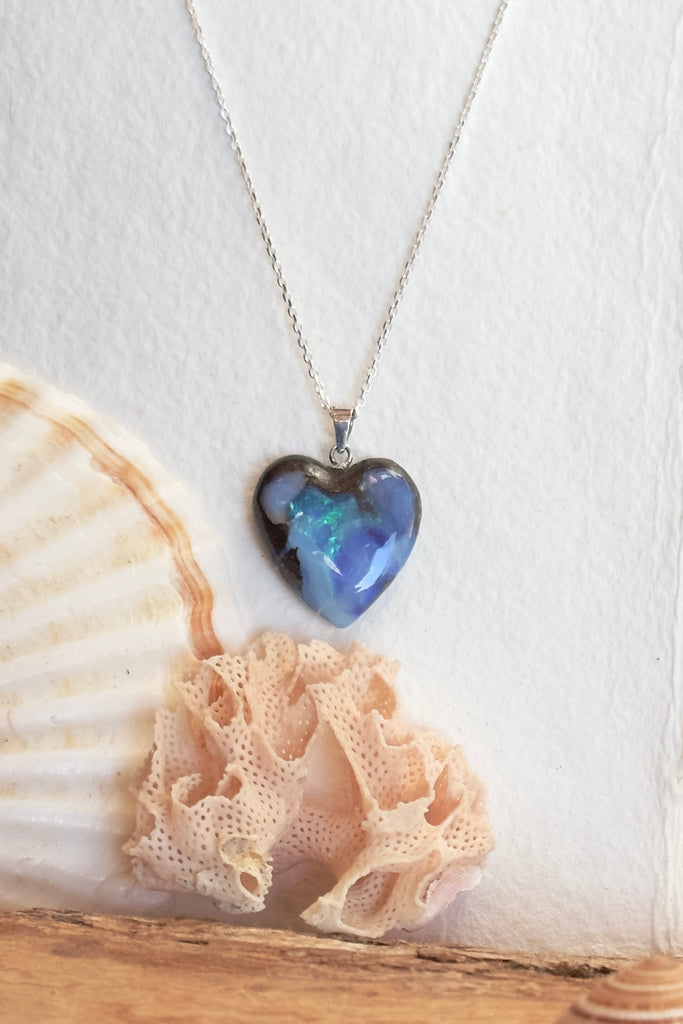 From our range of Australian opal pendants, an Australian solid boulder opal pendant in a heart shape, with crystalline detail that reveals bright flashes of blue green, dark blue and misty mauve. This piece has been cut into a soft heart shape