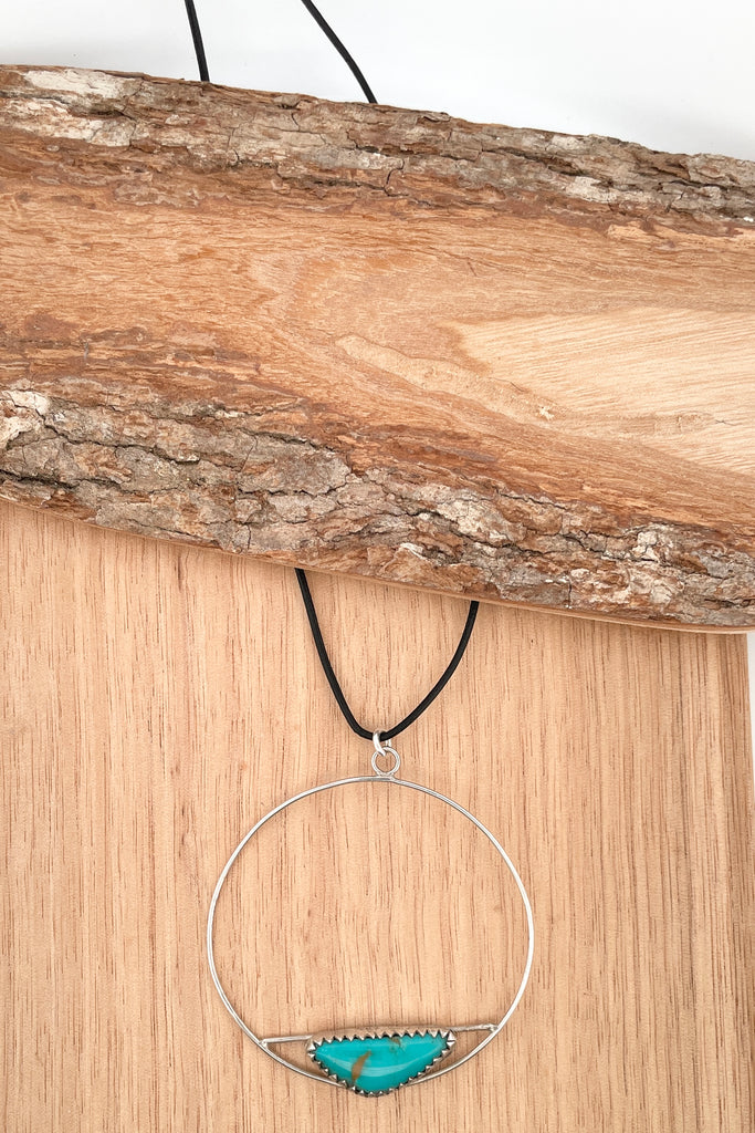 This lovely old turquoise pendant is a one off piece, hand carved into a freeform shape and showing the mark of the artist who designed it. Artisan set at the base of a hoop, it hangs from a simple black cord necklace. 