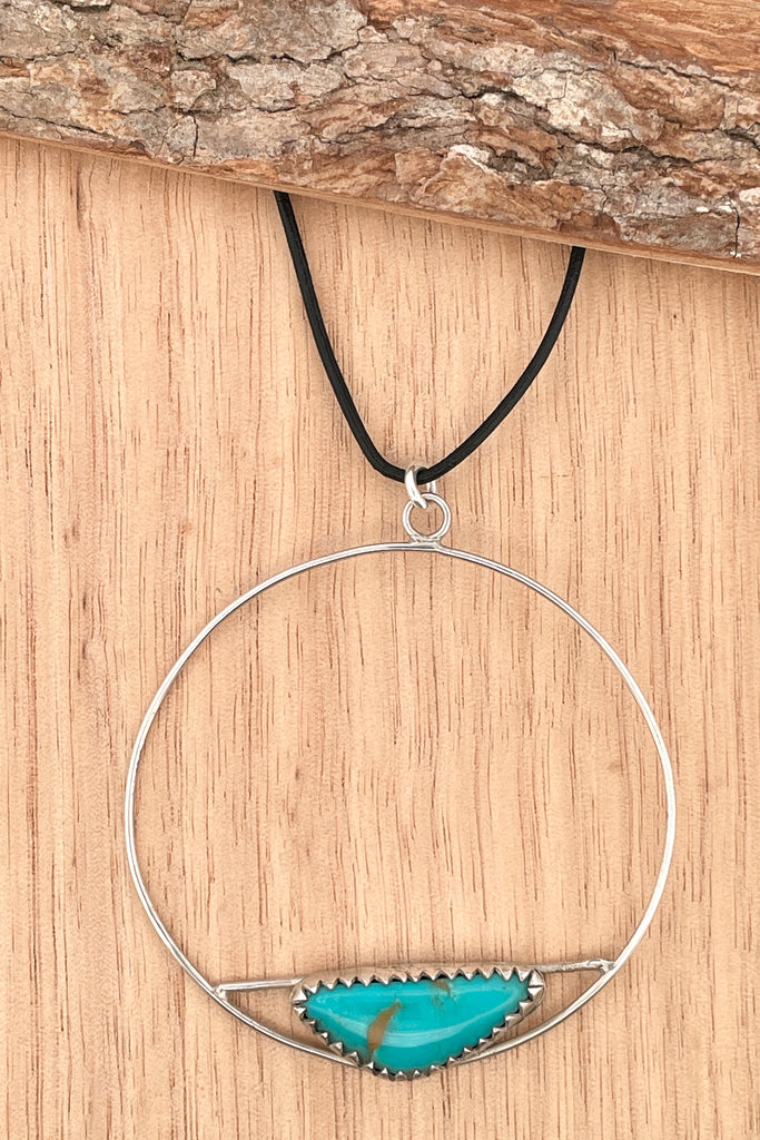 This lovely old turquoise pendant is a one off piece, hand carved into a freeform shape and showing the mark of the artist who designed it. Artisan set at the base of a hoop, it hangs from a simple black cord necklace. 