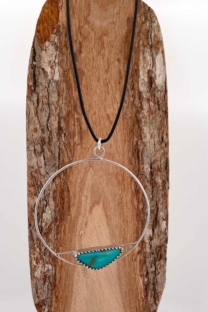 This lovely old turquoise pendant is a one off piece, hand carved into a freeform shape and showing the mark of the artist who designed it. Artisan set at the base of a hoop, it hangs from a simple black cord necklace. 