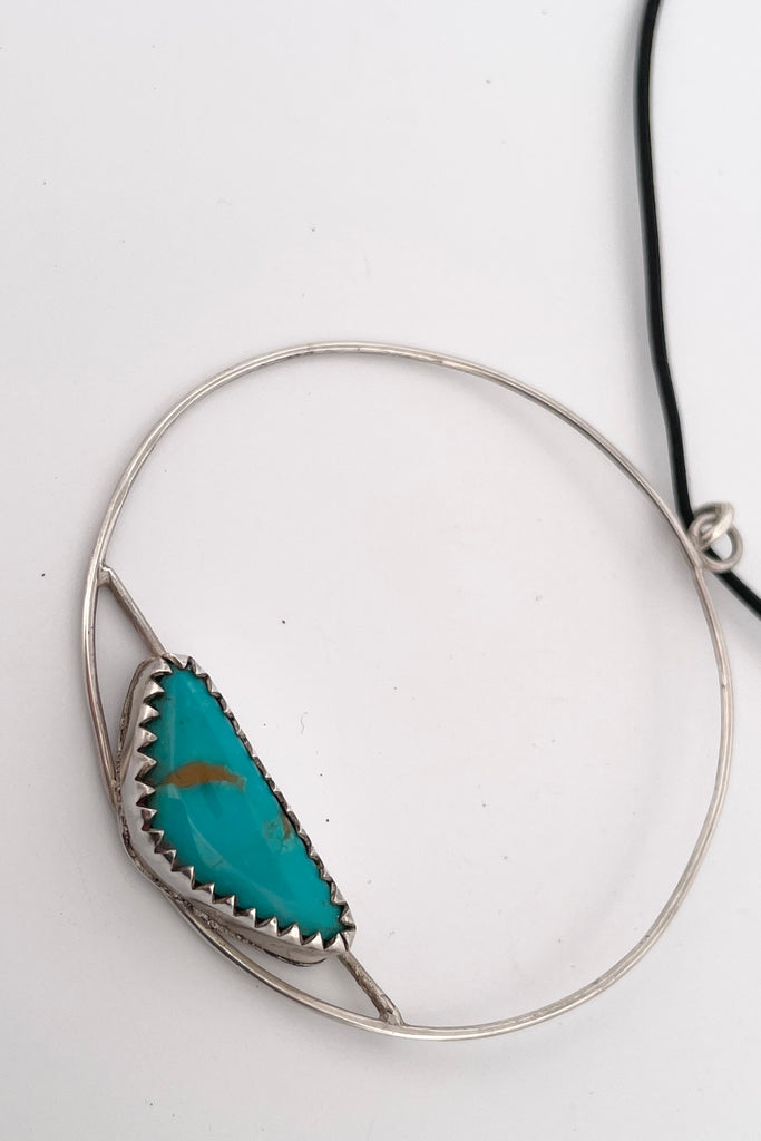 This lovely old turquoise pendant is a one off piece, hand carved into a freeform shape and showing the mark of the artist who designed it. Artisan set at the base of a hoop, it hangs from a simple black cord necklace. 