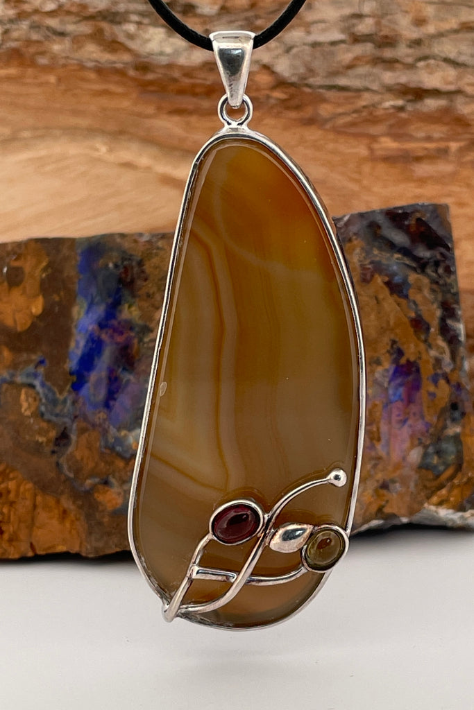 This unusual piece featuring a highly polished earth coloured Agate is set in silver, it has a decoration of two natural Tourmalie gemstones in the form of a flower.  Decorated with tiny Tourmaline Cabochons and silver foliage