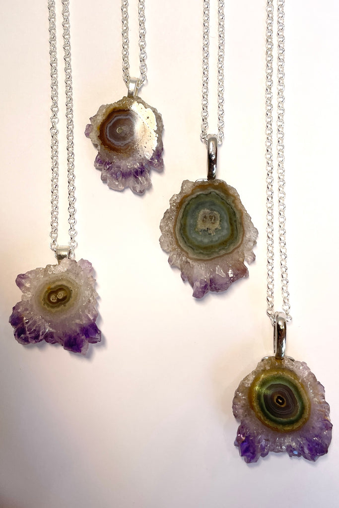 A lovely Amethyst druzy flower, pendant, cut as a slice with the crystal formations in the centre and the purple crystals at the base. It hangs from a  silvery chain. 