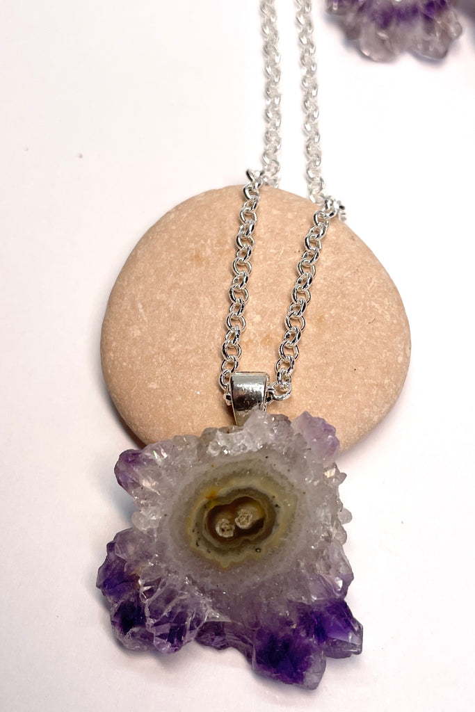 A lovely Amethyst druzy flower, pendant, cut as a slice with the crystal formations in the centre and the purple crystals at the base. It hangs from a  silvery chain. 