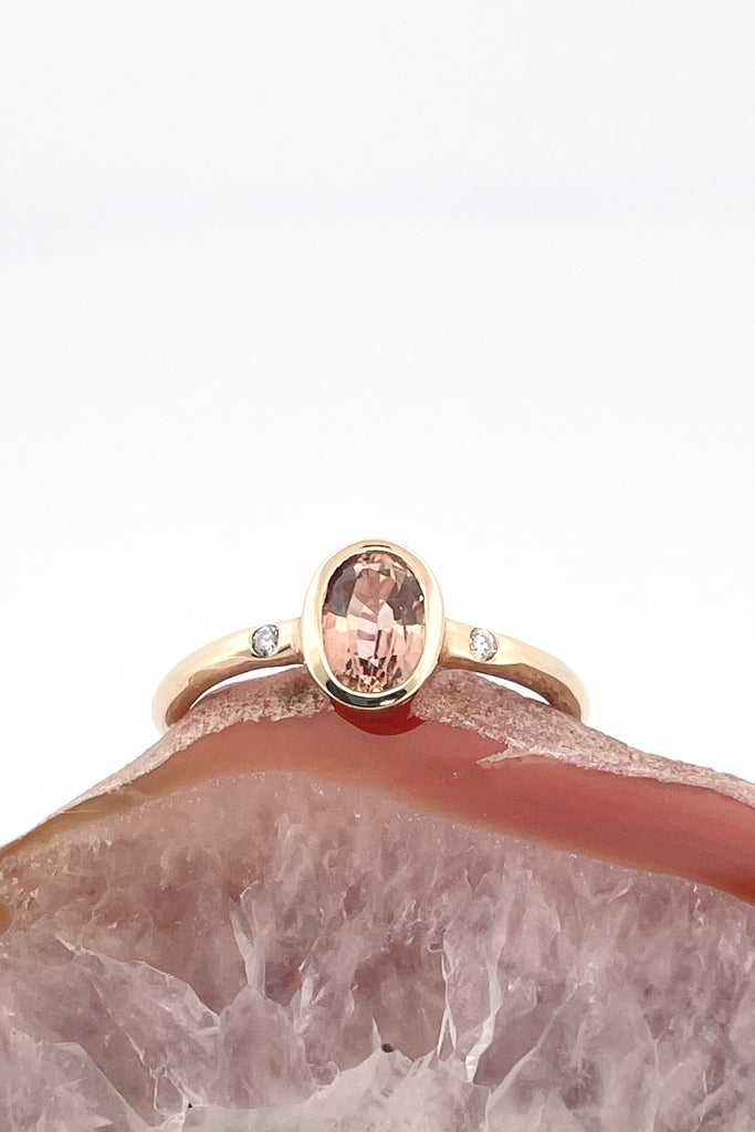 A beautiful simple ring designed to complement the lovely natural pale peach pink tourmaline gemstone set into the ring. The shank of the ring has a diamond on each side of the centre stone. 