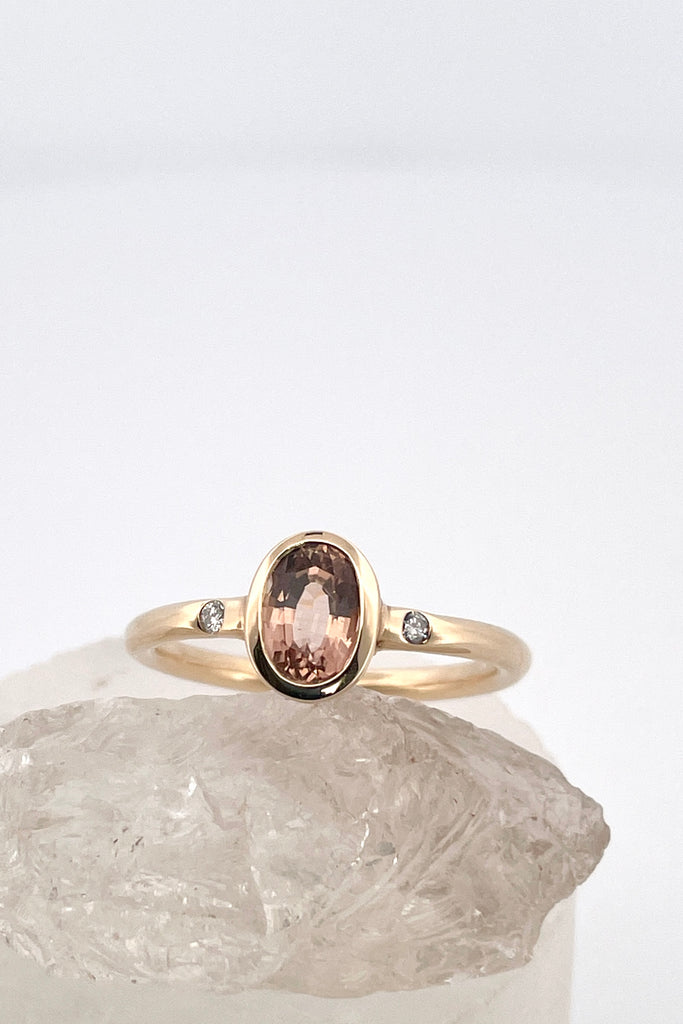 A beautiful simple ring designed to complement the lovely natural pale peach pink tourmaline gemstone set into the ring. The shank of the ring has a diamond on each side of the centre stone. 