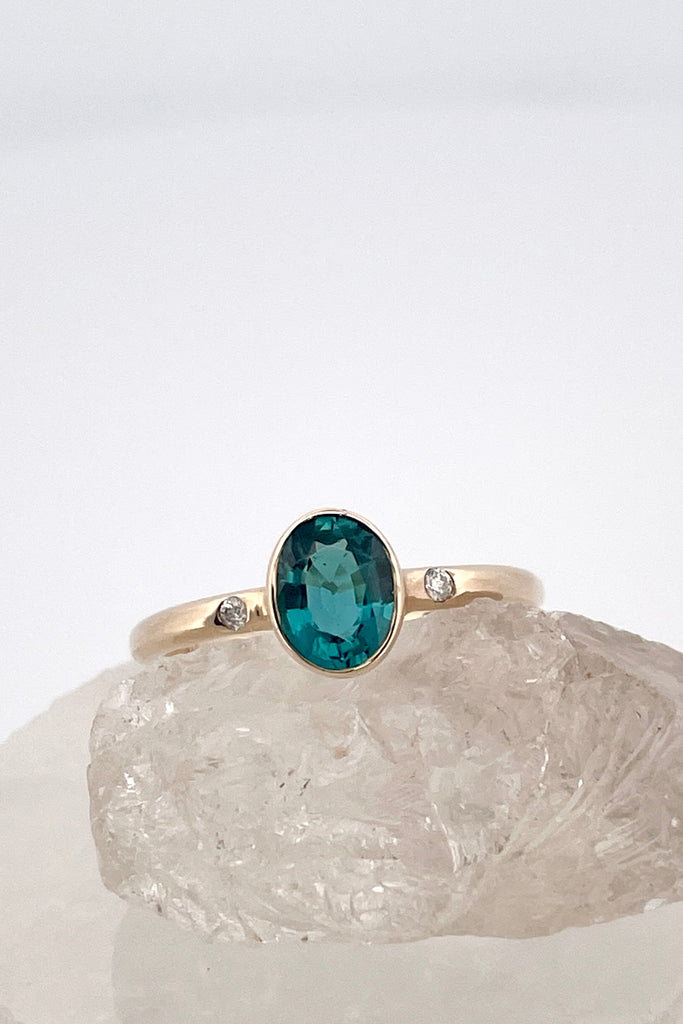 A beautiful simple ring designed to complement the lovely natural teal blue tourmaline gemstone set into the ring. The shank of the ring has a diamond on each side of the centre stone.