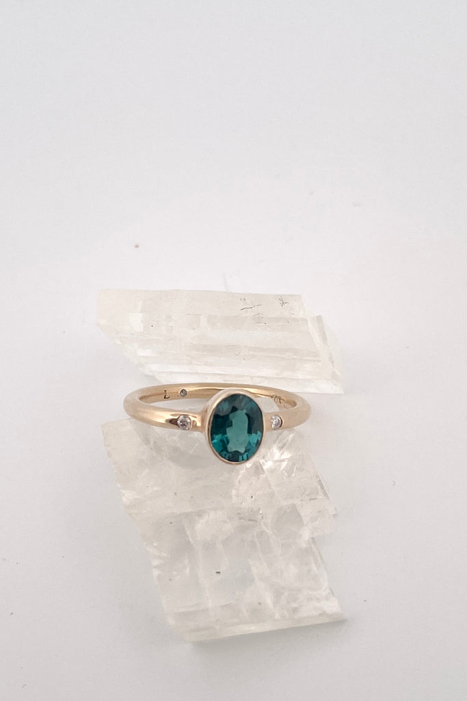 A beautiful simple ring designed to complement the lovely natural teal blue tourmaline gemstone set into the ring. The shank of the ring has a diamond on each side of the centre stone.