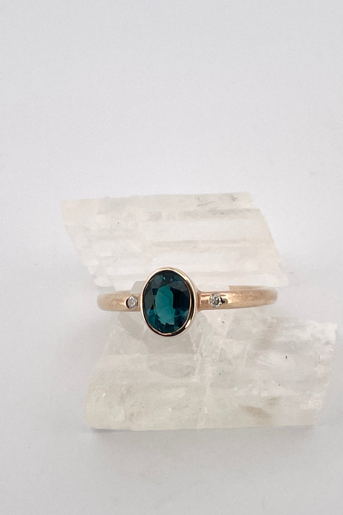 A beautiful simple ring designed to complement the lovely natural teal blue tourmaline gemstone set into the ring. The shank of the ring has a diamond on each side of the centre stone.