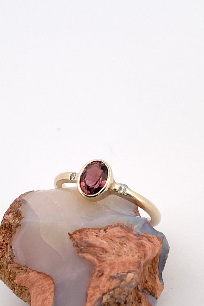 A beautiful simple ring designed to complement the lovely deep peachy red tourmaline gemstone set into the ring. The shank of the ring has a diamond on each side of the centre stone. 