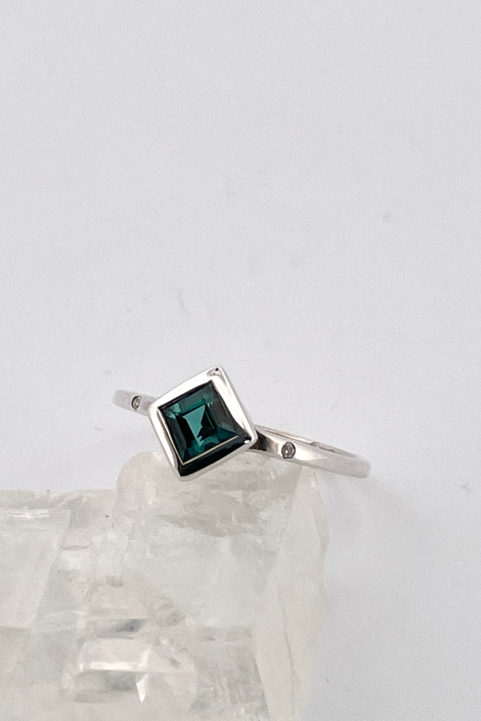 An elegant natural blue tourmaline ring with two small diamonds to accent the main stone. This ring comes with a tiny diamond set next to our signature "L" within the rings band. Natural Blue Nigerian Tourmaline responsibly sourced.