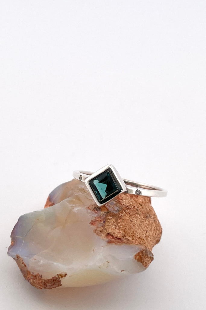 An elegant natural blue tourmaline ring with two small diamonds to accent the main stone. This ring comes with a tiny diamond set next to our signature "L" within the rings band. Natural Blue Nigerian Tourmaline responsibly sourced.