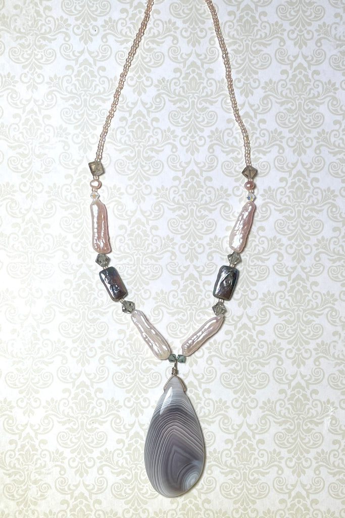 The centre piece is a wonderful misty grey and white banded Agate cut in a freeform droplet shape that enhances the curves of the stone. The necklace is made with four lovely pale pink pearls, two irredescent grey pearls, smoky quartz beads and swarovski crystal beads. 