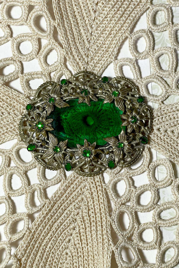 A brooch from the Edwardian era, it features a lovely emerald green centre piece and small green rhinestones that are all claw set with none missing. 