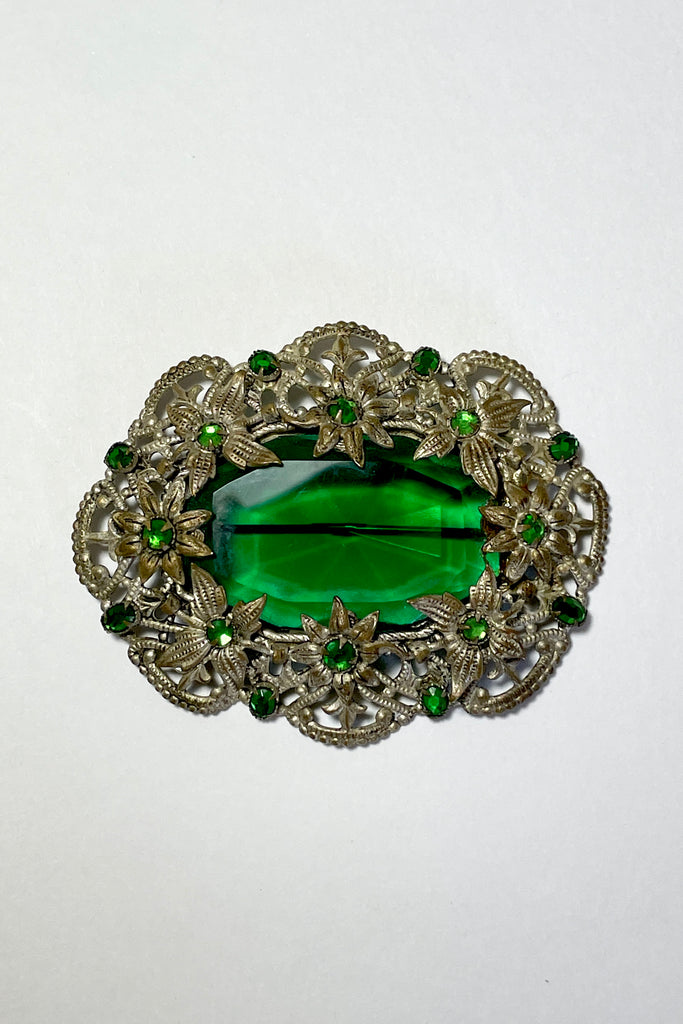 A brooch from the Edwardian era, it features a lovely emerald green centre piece and small green rhinestones that are all claw set with none missing. 