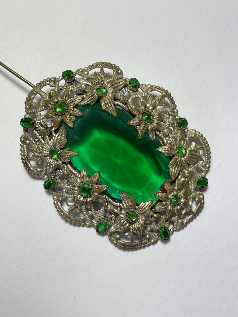 A brooch from the Edwardian era, it features a lovely emerald green centre piece and small green rhinestones that are all claw set with none missing. 
