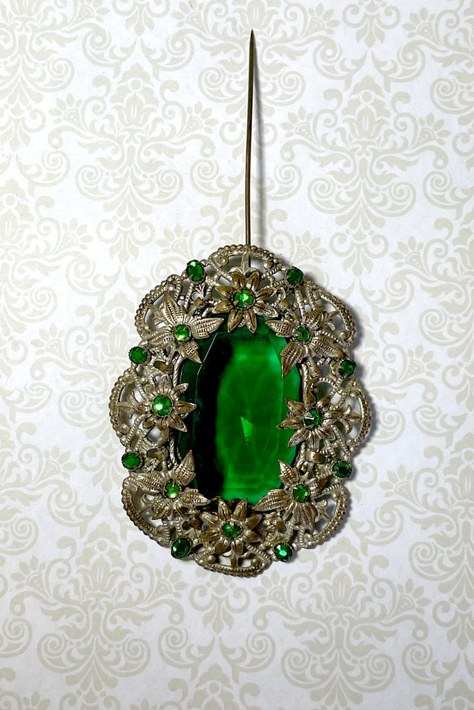 A brooch from the Edwardian era, it features a lovely emerald green centre piece and small green rhinestones that are all claw set with none missing. 