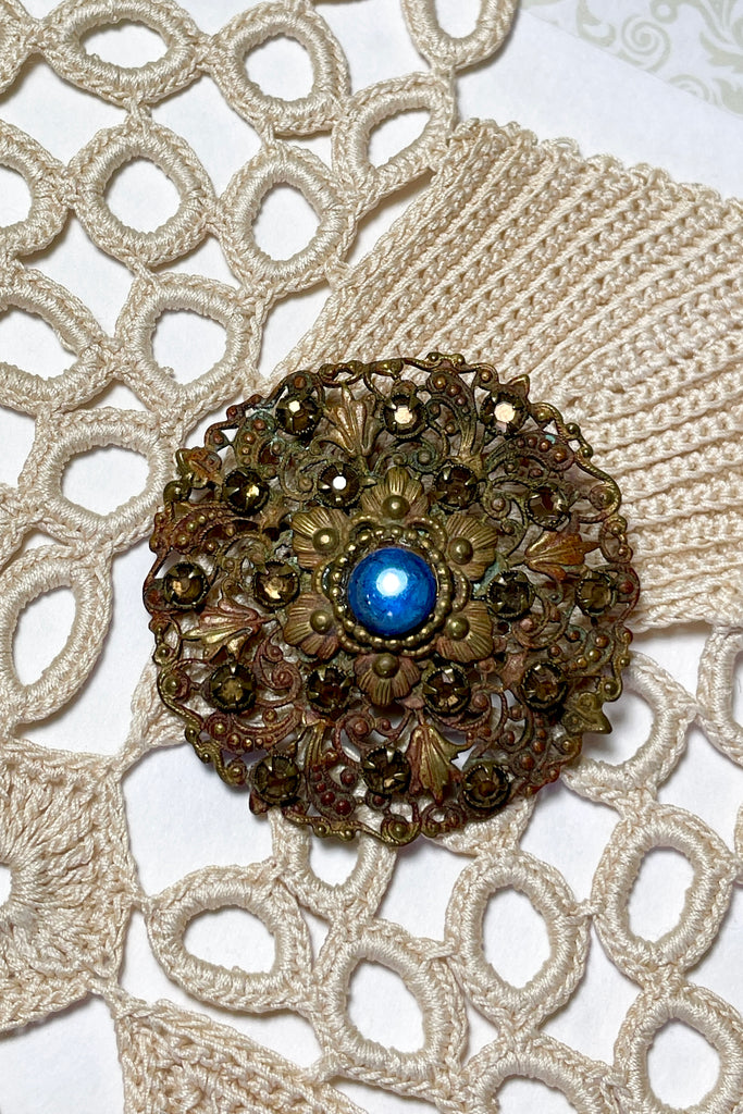 From the Edwardian era, it features a centre blue cabochon rhinestone in the centre and smaller antique gold colour stones that are all claw set with none missing. This is a piece that has a mysterious historical vibe. Good condition for it's age.
