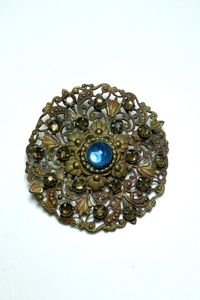 From the Edwardian era, it features a centre blue cabochon rhinestone in the centre and smaller antique gold colour stones that are all claw set with none missing. This is a piece that has a mysterious historical vibe. Good condition for it's age.