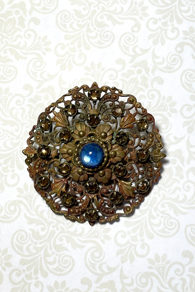 From the Edwardian era, it features a centre blue cabochon rhinestone in the centre and smaller antique gold colour stones that are all claw set with none missing. This is a piece that has a mysterious historical vibe. Good condition for it's age.