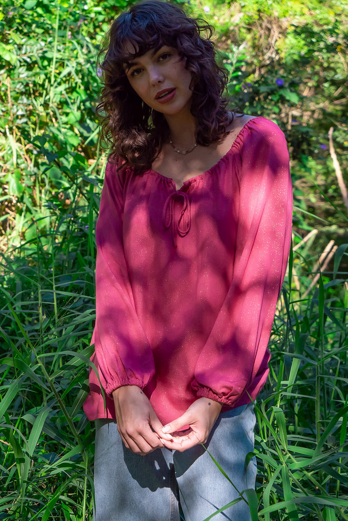 The Joni Berry Sparkle Boho Blouse is a beautiful deep pink blouse with a gold lurex shimmer all throughout. The blouse features a drawstring neckline with front keyhole and long sleeves with elasticated cuffs. Made from a woven blend of rayon, lurex, mulberry silk, and modal.