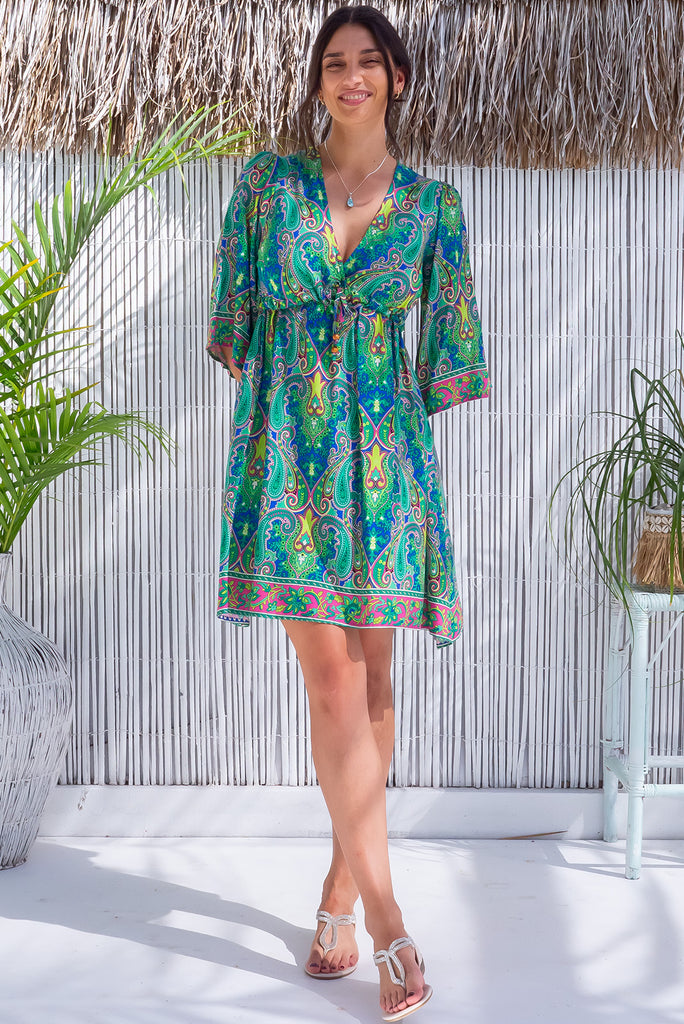 The Layla Jazzy Green Mini Dress is a vibrant mini dress with a blue base and green and pink paisley print. The dress features flutter sleeves, empire line drawstring and side pockets. Made from 100% rayon.