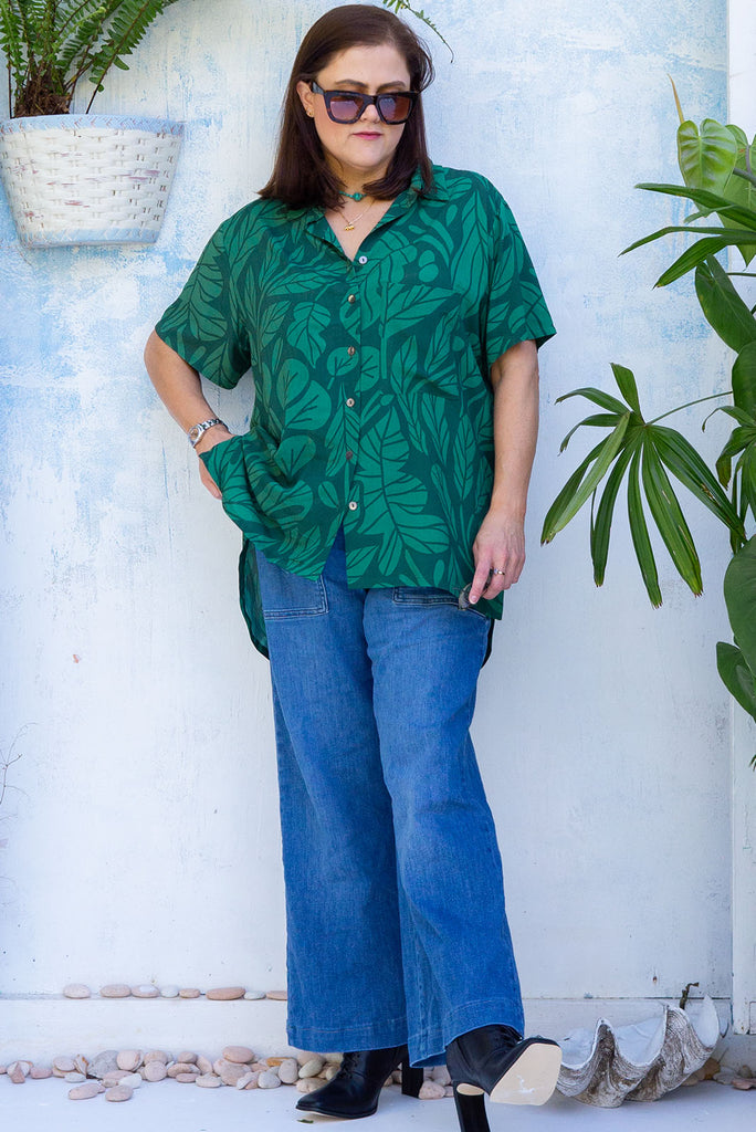 The Leonora Botany Green Short Sleeve Shirt is a tonal green relaxed fit button down shirt with botanical leaf print. The blouse features short sleeves, button down front, classic collar, one bust pocket, side slits, scooped hem at sides and slightly longer back. Made from woven 100% rayon.