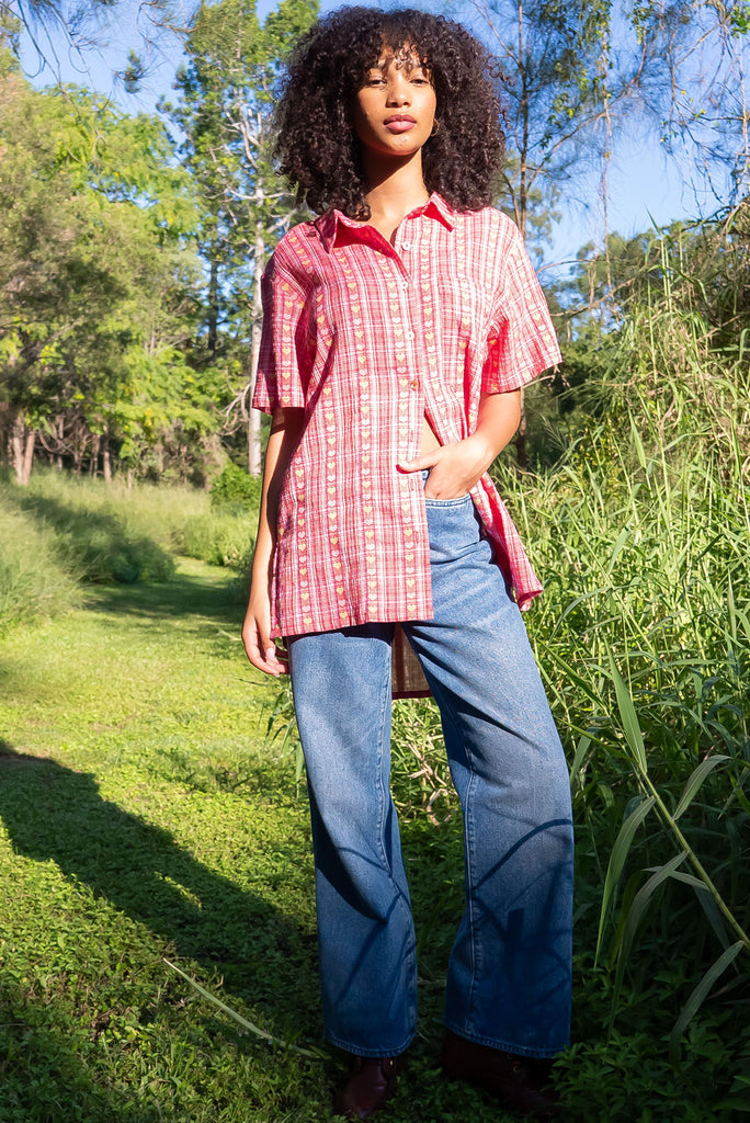 The Leonora Botany Green Short Sleeve Shirt is a plaid pink, relaxed fit, button down shirt with embroidered hearts in pink and orange. The blouse features short sleeves, button down front, classic collar, one bust pocket, side slits, scooped hem at sides and slightly longer back. Made from woven blend of cotton and polyester. 