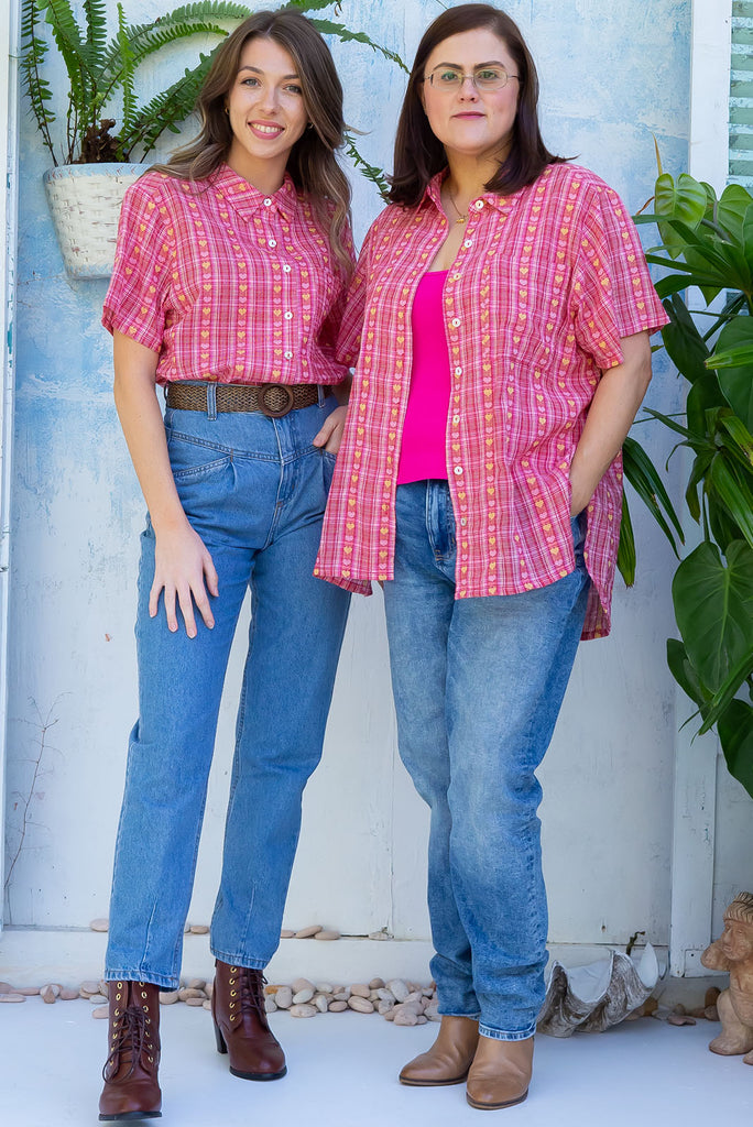 The Leonora Botany Green Short Sleeve Shirt is a plaid pink, relaxed fit, button down shirt with embroidered hearts in pink and orange. The blouse features short sleeves, button down front, classic collar, one bust pocket, side slits, scooped hem at sides and slightly longer back. Made from woven blend of cotton and polyester. 