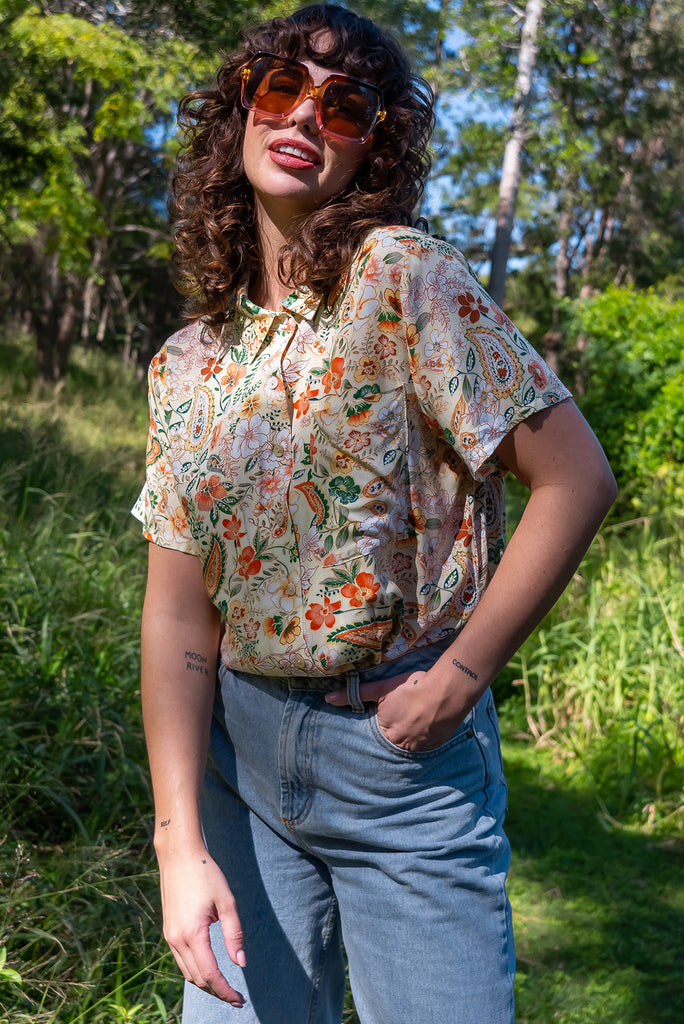 The Leonora The Florist Shirt is a gorgeous pale yellow button up shirt with a floral paisley print. The blouse features short sleeves, button down front, classic collar, one bust pocket, side slits, scooped hem at sides and slightly longer back. Made from woven 100% rayon.