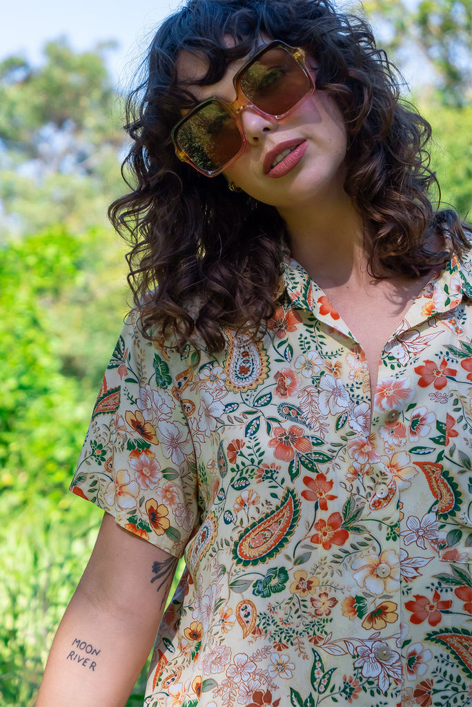 The Leonora The Florist Shirt is a gorgeous pale yellow button up shirt with a floral paisley print. The blouse features short sleeves, button down front, classic collar, one bust pocket, side slits, scooped hem at sides and slightly longer back. Made from woven 100% rayon.