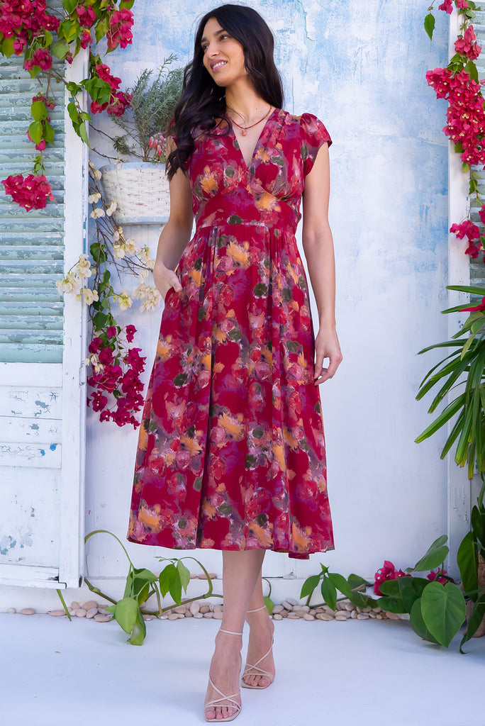 The Lizzie Artista Red Midi Dress is a beautiful red based dress with a watercolour floral print. The dress features cap sleeves, a deep v neckline, fitted Basque waist with gathered bust, elastic shirring at back waist, side pockets and is made from woven 100% rayon.