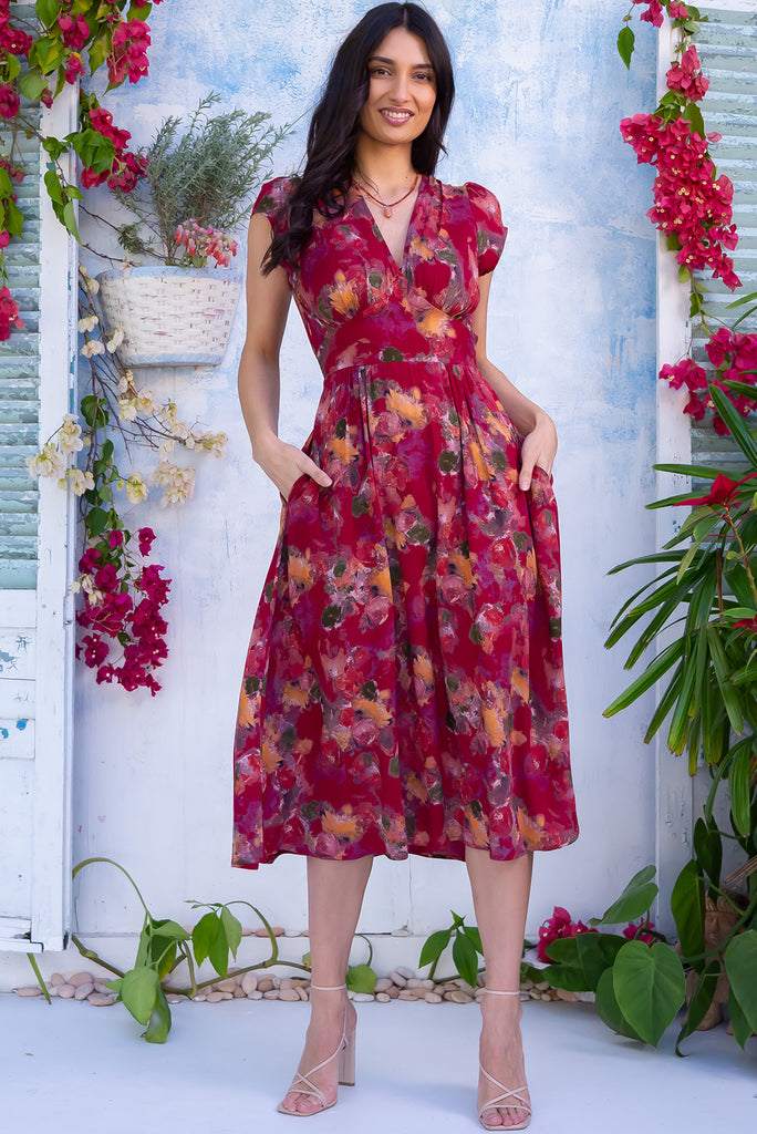 The Lizzie Artista Red Midi Dress is a beautiful red based dress with a watercolour floral print. The dress features cap sleeves, a deep v neckline, fitted Basque waist with gathered bust, elastic shirring at back waist, side pockets and is made from woven 100% rayon.