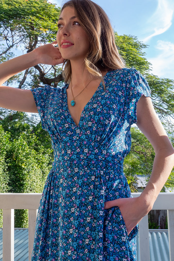 The Lizzie Blue Tea Rose Dress is a beautiful black dress with a blue ditty floral print. The dress features cap sleeves, a deep v neckline, fitted Basque waist with gathered bust, elastic shirring at back waist, side pockets and is made from woven 100% rayon.