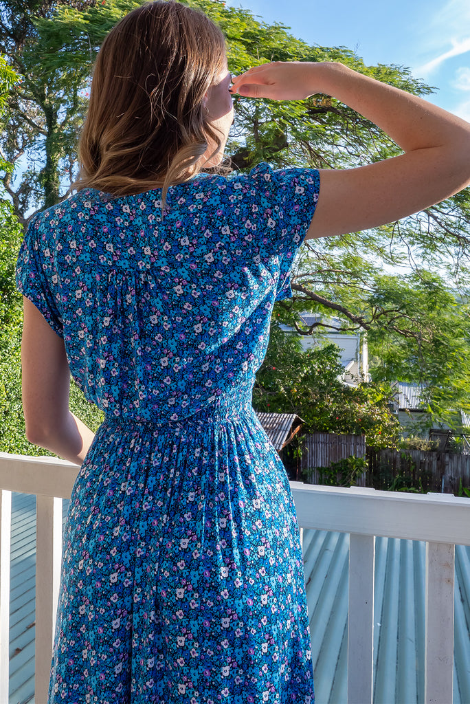 The Lizzie Blue Tea Rose Dress is a beautiful black dress with a blue ditty floral print. The dress features cap sleeves, a deep v neckline, fitted Basque waist with gathered bust, elastic shirring at back waist, side pockets and is made from woven 100% rayon.
