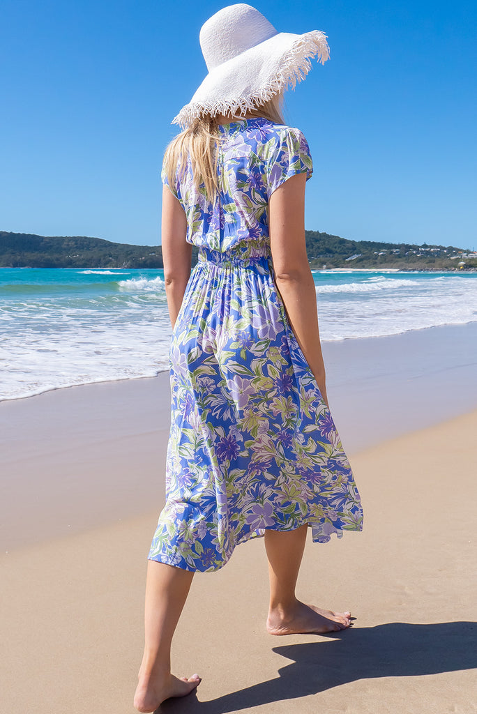 The Lizzie Cornflower Blue Midi Dress is a beautiful blue based dress with a white and green, large floral print. The dress features cap sleeves, a deep v neckline, fitted Basque waist with gathered bust, elastic shirring at back waist, side pockets and is made from woven 100% rayon.