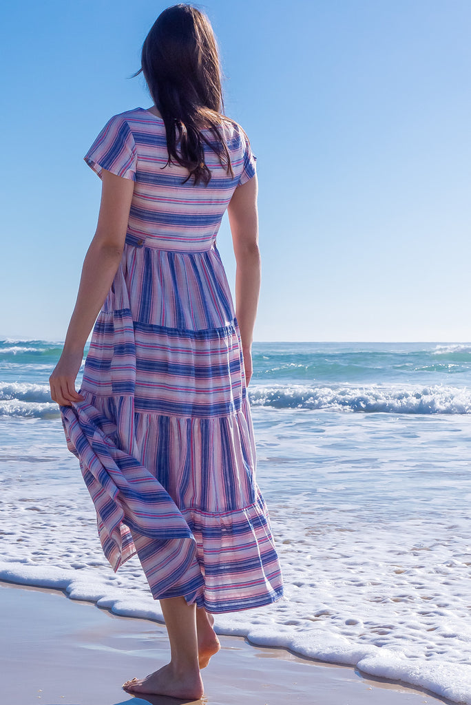 The Louisa Soft Light Stripes Maxi Dress is a beautiful tiered maxi dress with blue, white, and pink stripes. This dress features a scooped neckline, adjustable waist tabs, side pockets and a wide tiered skirt. Made from a woven blend of cotton and polyester.