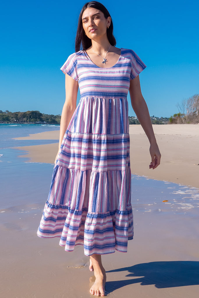 The Louisa Soft Light Stripes Maxi Dress is a beautiful tiered maxi dress with blue, white, and pink stripes. This dress features a scooped neckline, adjustable waist tabs, side pockets and a wide tiered skirt. Made from a woven blend of cotton and polyester.