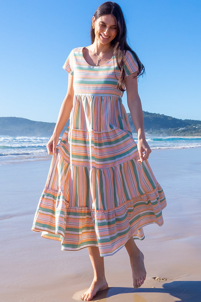 The Louisa Summer Sun Stripes Maxi Dress is a beautiful tiered maxi dress with green, white, orange and yellow stripes. This dress features a scooped neckline, adjustable waist tabs, side pockets and a wide tiered skirt. Made from a woven blend of cotton and polyester.