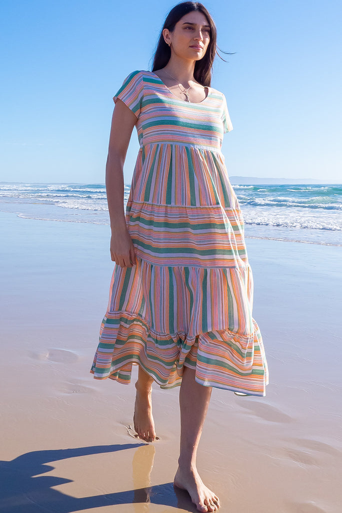 The Louisa Summer Sun Stripes Maxi Dress is a beautiful tiered maxi dress with green, white, orange and yellow stripes. This dress features a scooped neckline, adjustable waist tabs, side pockets and a wide tiered skirt. Made from a woven blend of cotton and polyester.