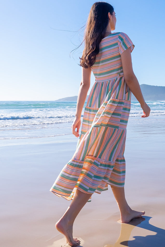 The Louisa Summer Sun Stripes Maxi Dress is a beautiful tiered maxi dress with green, white, orange and yellow stripes. This dress features a scooped neckline, adjustable waist tabs, side pockets and a wide tiered skirt. Made from a woven blend of cotton and polyester.