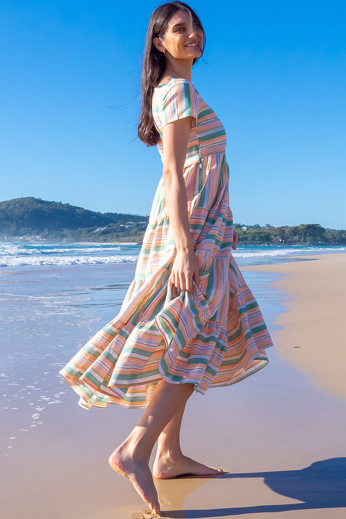 The Louisa Summer Sun Stripes Maxi Dress is a beautiful tiered maxi dress with green, white, orange and yellow stripes. This dress features a scooped neckline, adjustable waist tabs, side pockets and a wide tiered skirt. Made from a woven blend of cotton and polyester.