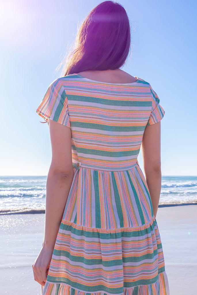The Louisa Summer Sun Stripes Maxi Dress is a beautiful tiered maxi dress with green, white, orange and yellow stripes. This dress features a scooped neckline, adjustable waist tabs, side pockets and a wide tiered skirt. Made from a woven blend of cotton and polyester.